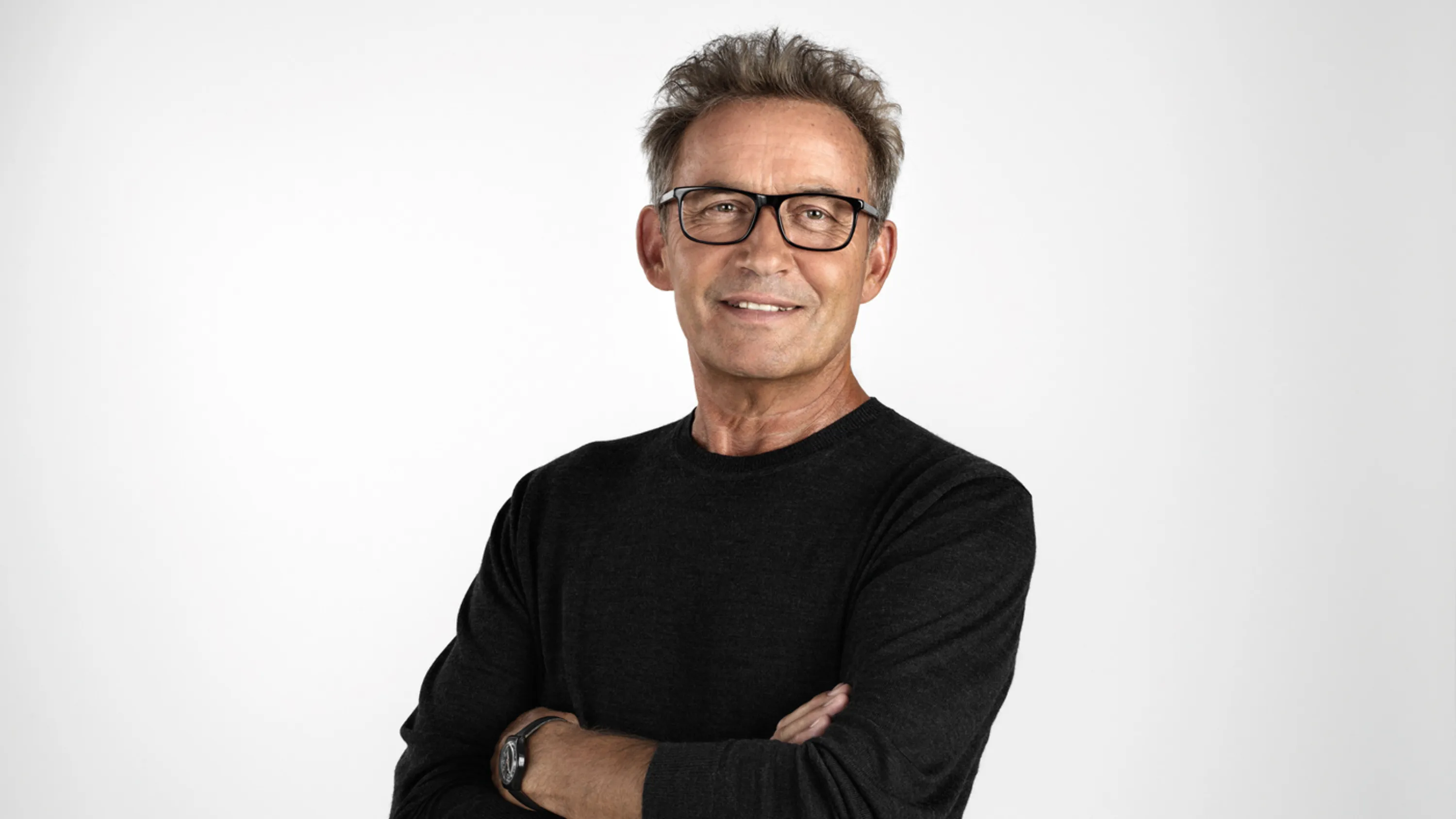 Un homme âgé, les bras croisés, sourit