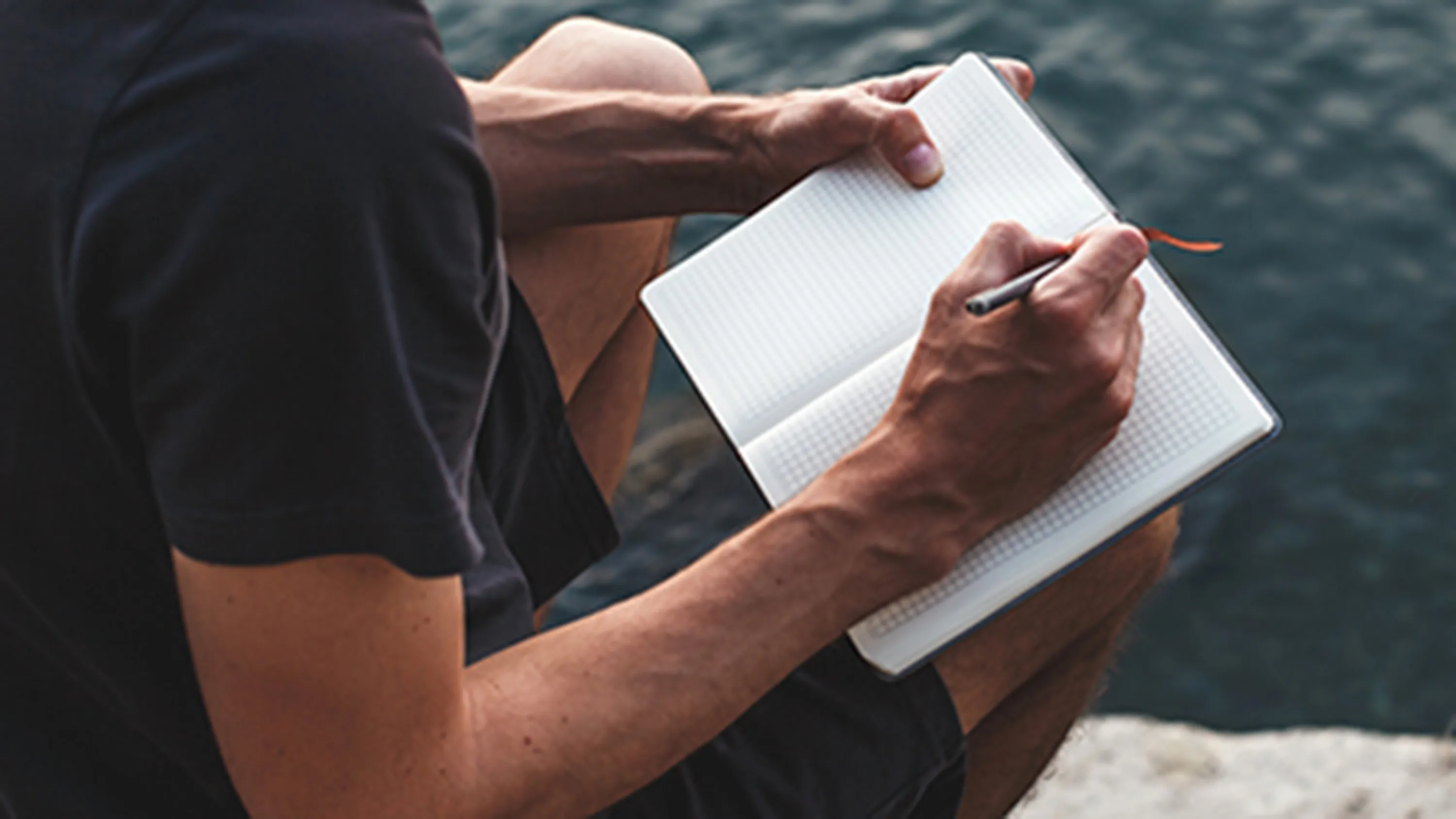 Un monsieur écrit dans un carnet en regardant le lac.