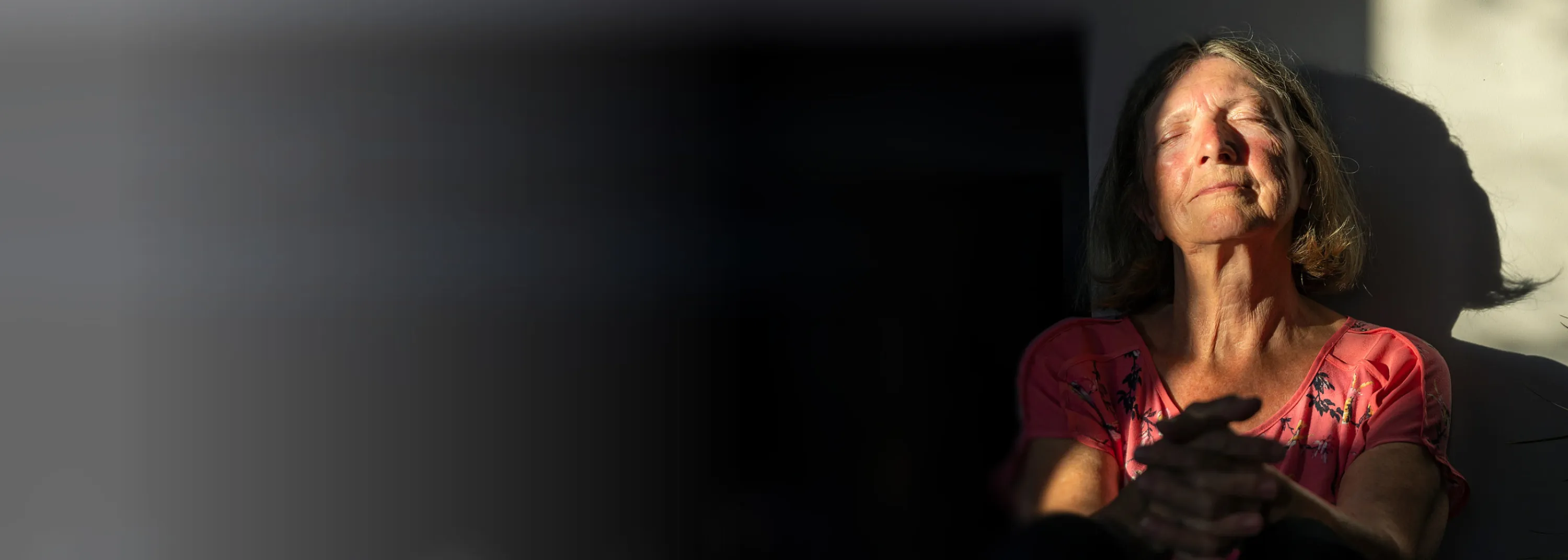 Eine ältere Dame sitzt mit gelassenem Blick in einem Zimmer.