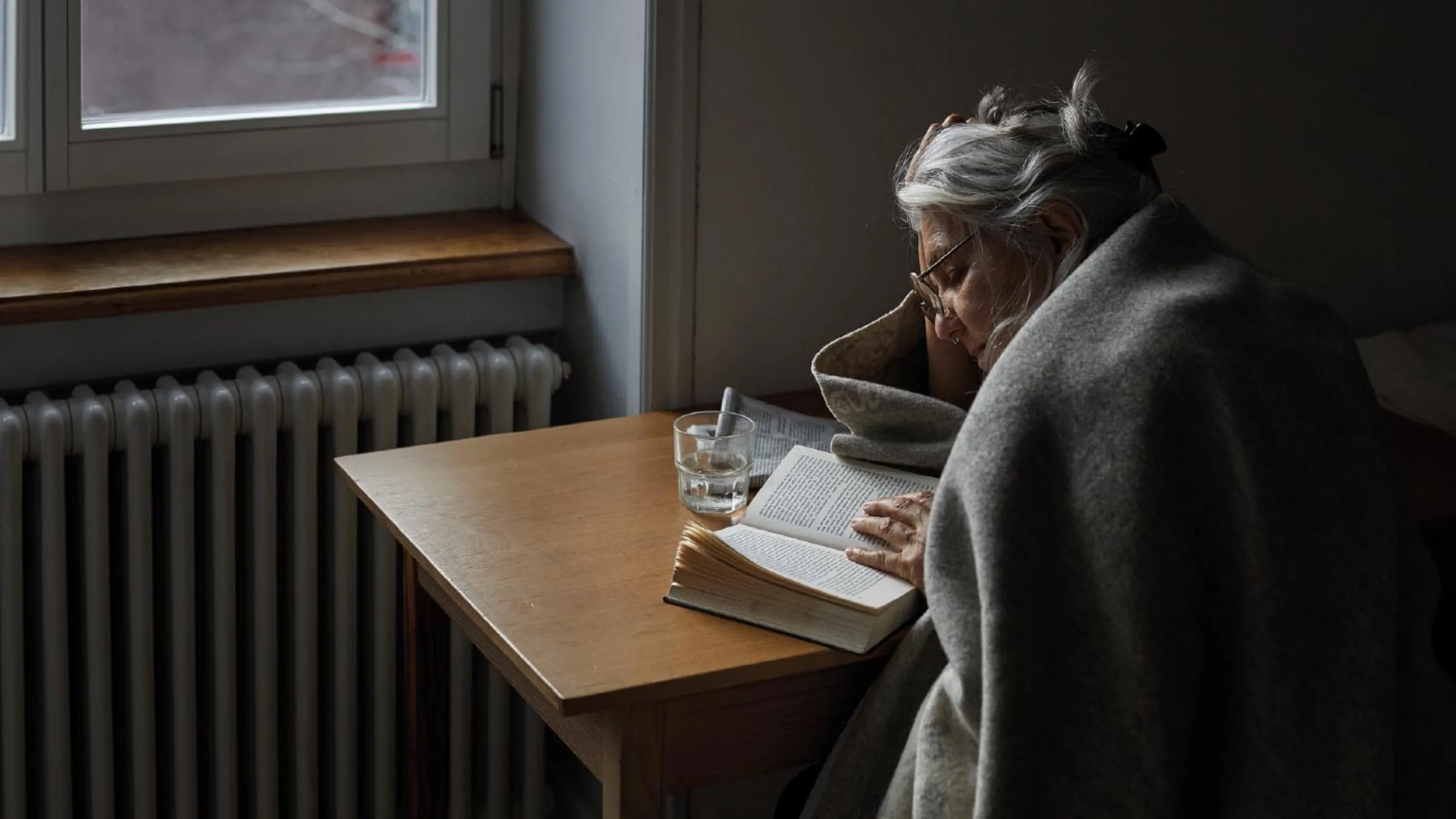 Eine Seniorin mit Decke und Tee liest ein Buch.